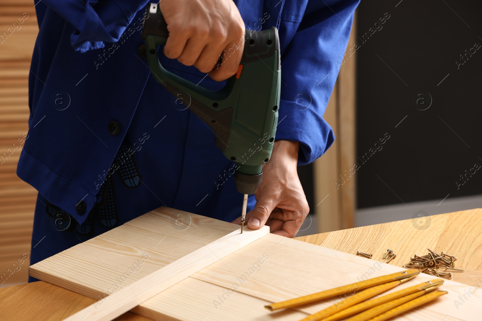 Professional repairman twisting screw into wooden plank with electric screwdriver indoors, closeup Photo of Professional repairman twisting screw into wooden plank with electric screwdriver indoors, closeup