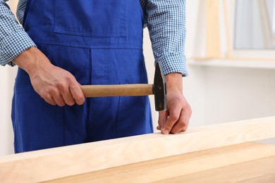 Photo of Professional repairman hammering nail into wooden plank indoors, closeup