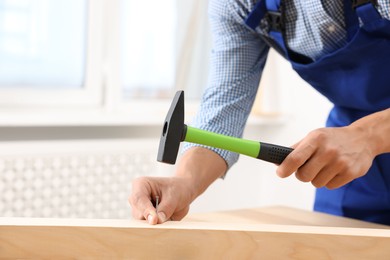 Photo of Professional repairman hammering nail into wooden plank indoors, closeup. Space for text