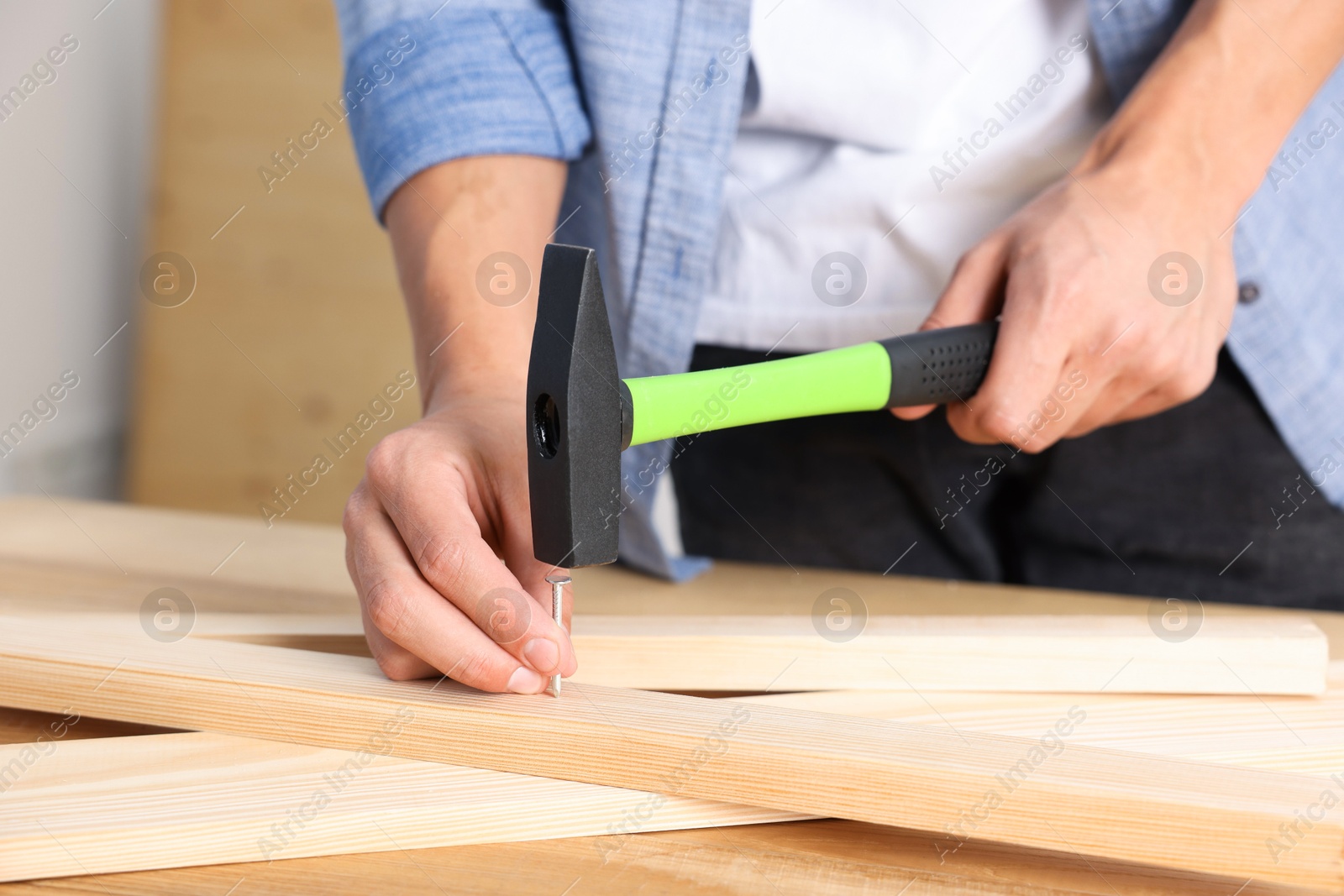 Photo of Man hammering nail into wooden plank indoors, closeup