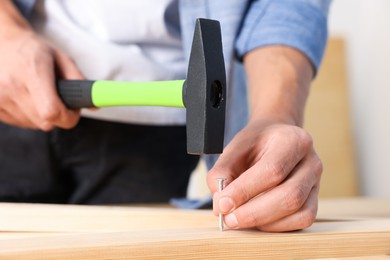 Photo of Man hammering nail into wooden plank indoors, closeup