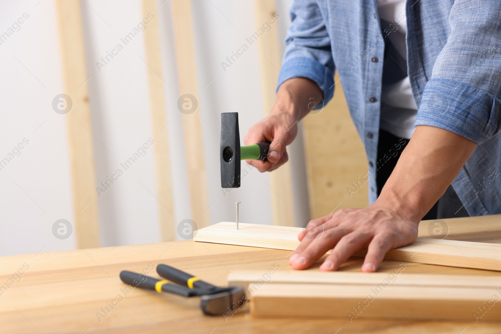 Man hammering nail into wooden plank indoors, closeup. Space for text Photo of Man hammering nail into wooden plank indoors, closeup. Space for text