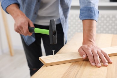 Photo of Man hammering nail into wooden plank indoors, closeup