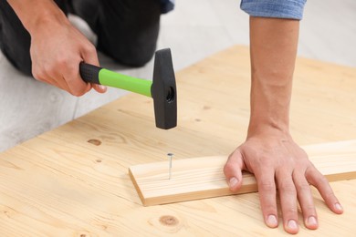 Photo of Man hammering nail into wooden plank indoors, closeup