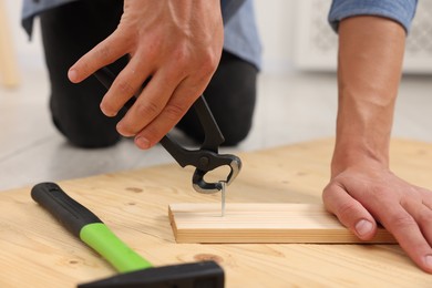 Photo of Man pulling metal nail out of wooden plank with pincers indoors, closeup
