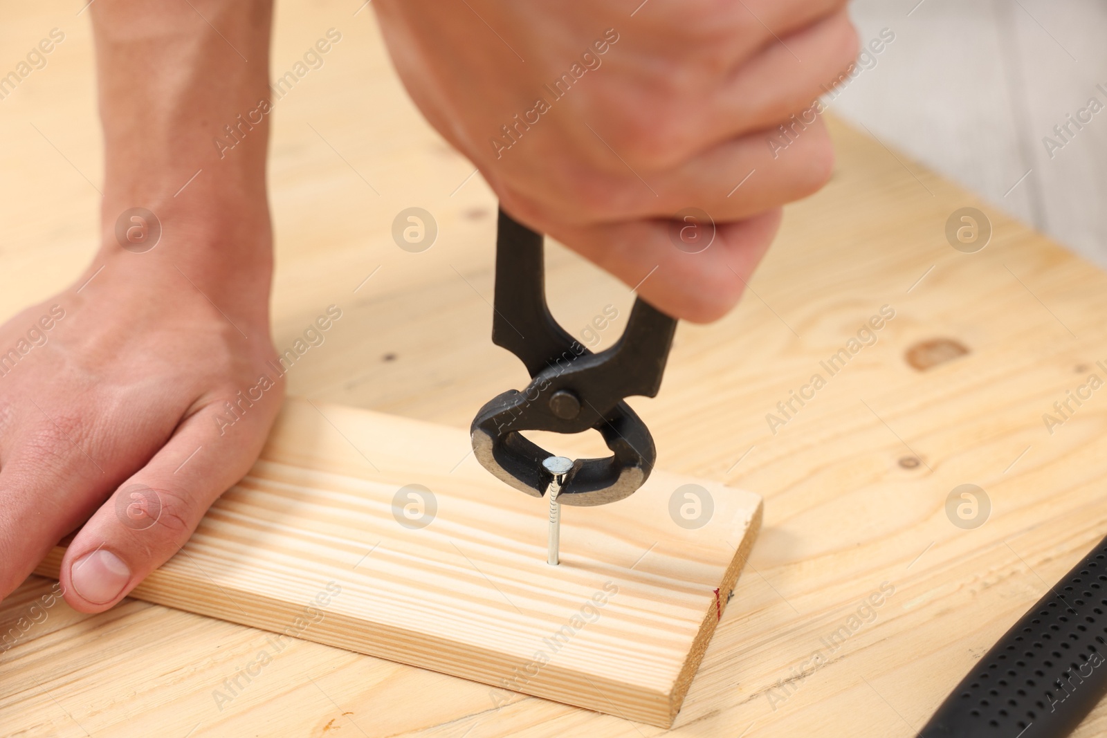 Man pulling metal nail out of wooden plank with pincers indoors, closeup Photo of Man pulling metal nail out of wooden plank with pincers indoors, closeup