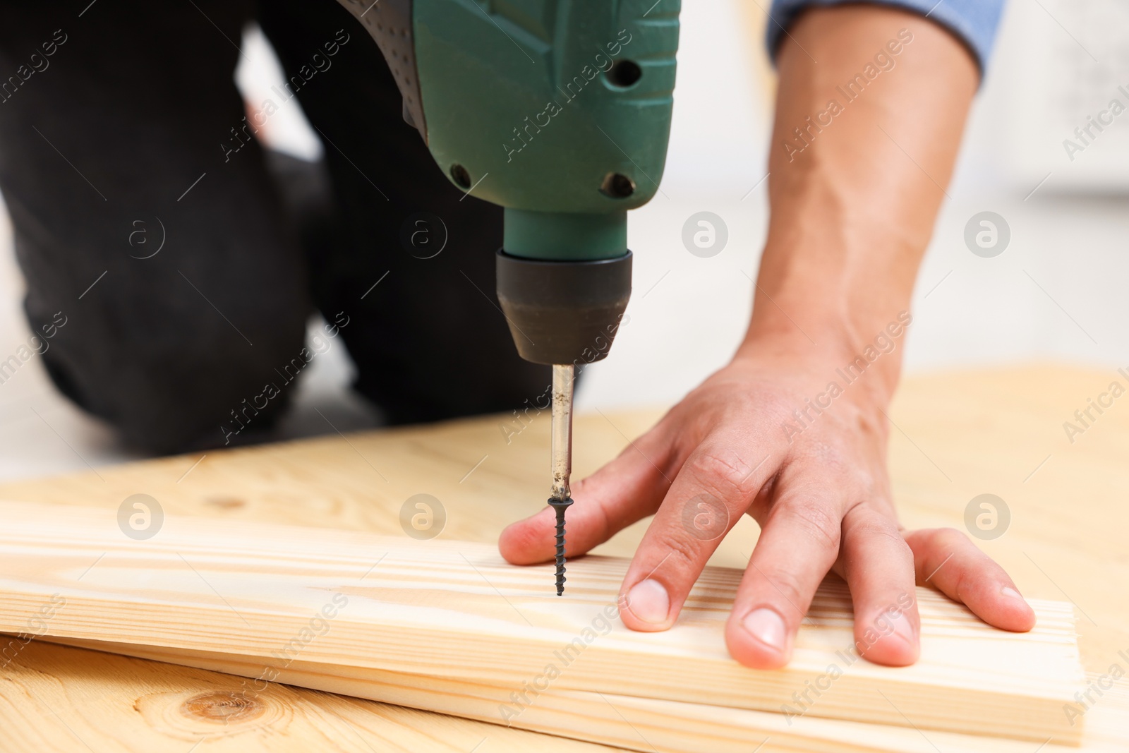 Professional repairman twisting screw into wooden plank with electric screwdriver indoors, closeup Photo of Professional repairman twisting screw into wooden plank with electric screwdriver indoors, closeup
