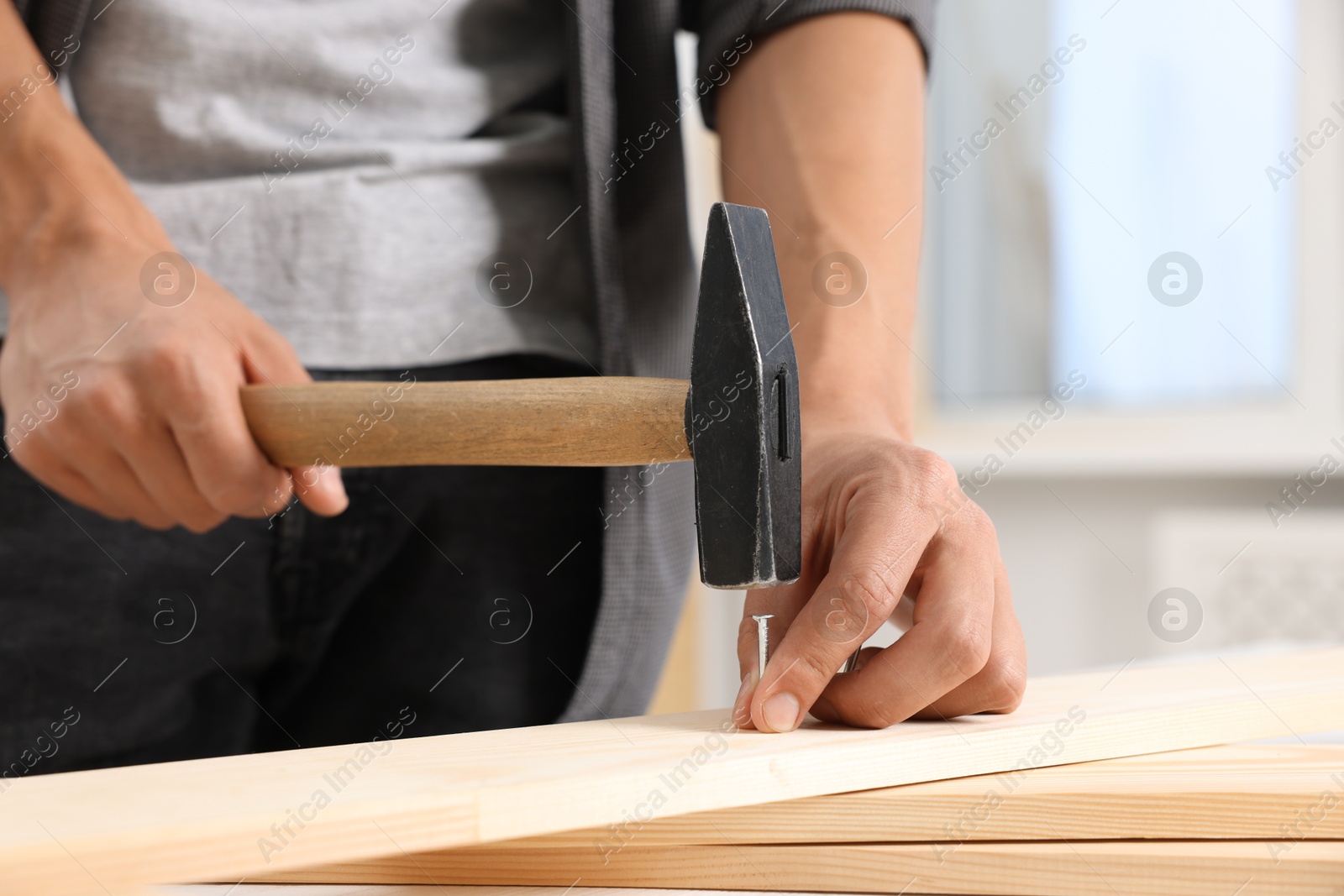 Photo of Man hammering nail into wooden plank indoors, closeup
