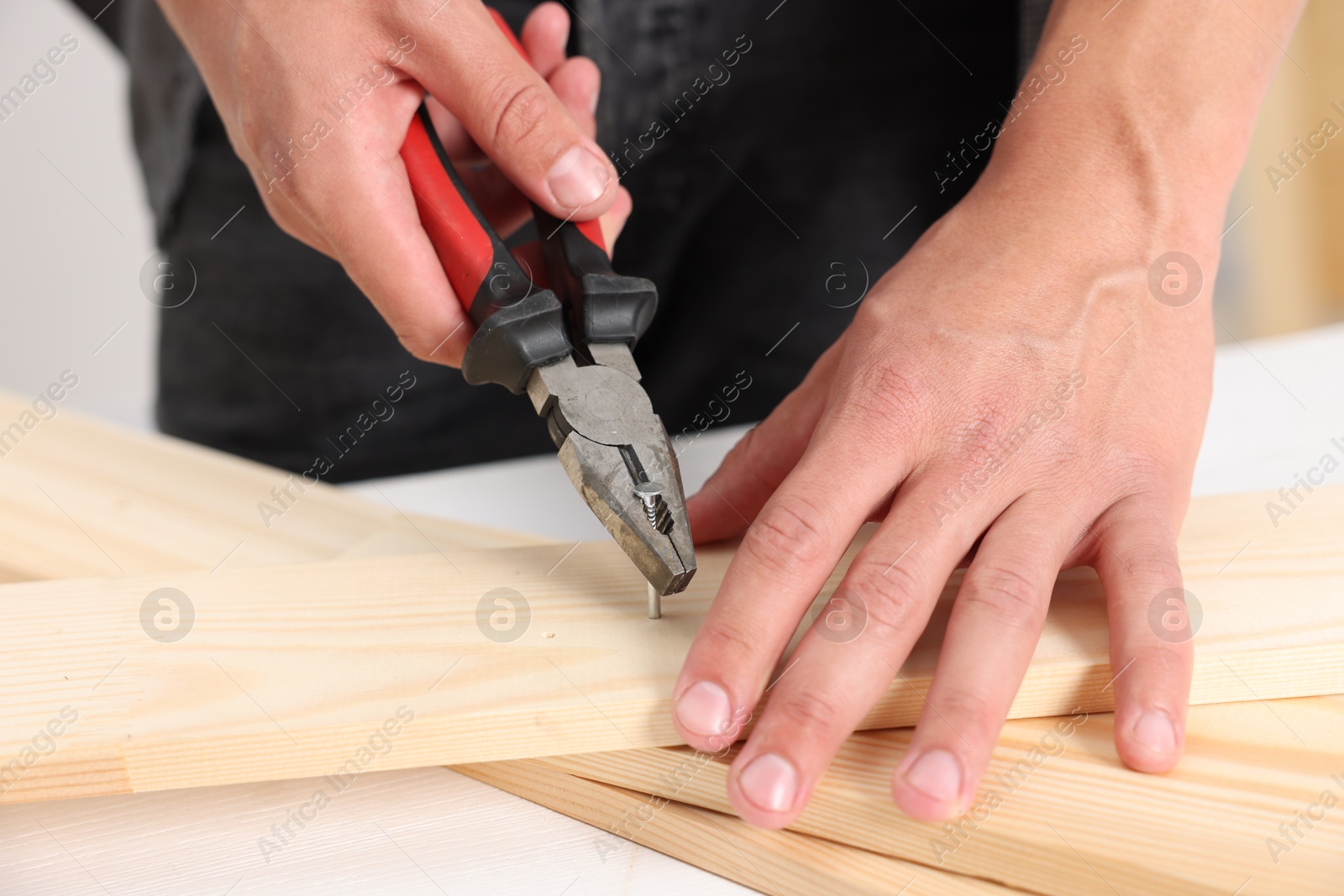 Man pulling metal nail out of wooden plank with pincers indoors, closeup Photo of Man pulling metal nail out of wooden plank with pincers indoors, closeup