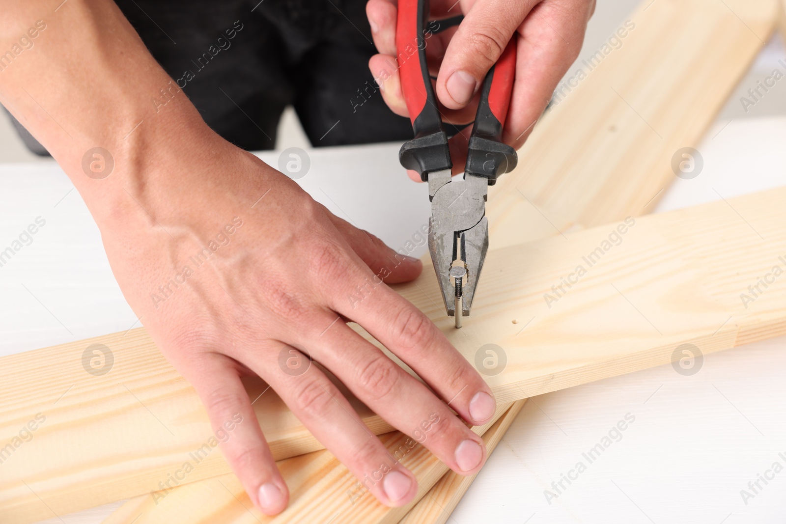 Man pulling metal nail out of wooden plank with pincers indoors, closeup Photo of Man pulling metal nail out of wooden plank with pincers indoors, closeup