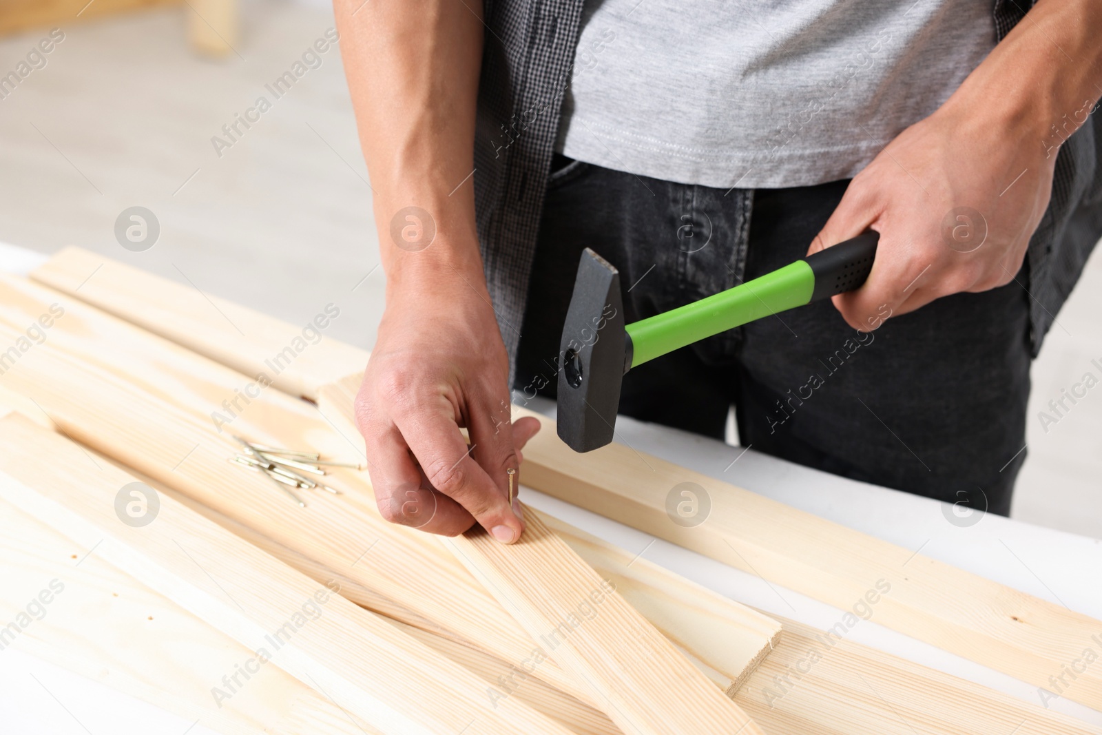 Photo of Man hammering nail into wooden plank indoors, closeup