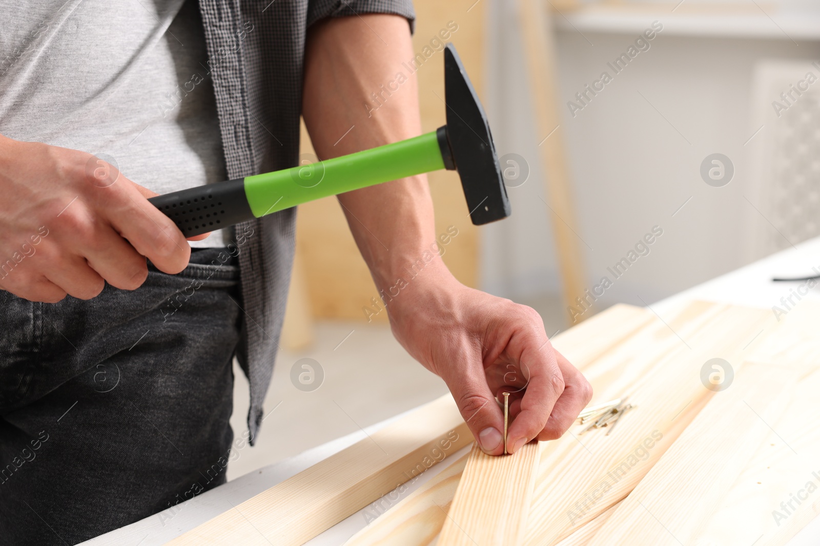 Photo of Man hammering nail into wooden plank indoors, closeup. Space for text
