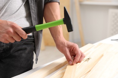 Photo of Man hammering nail into wooden plank indoors, closeup. Space for text