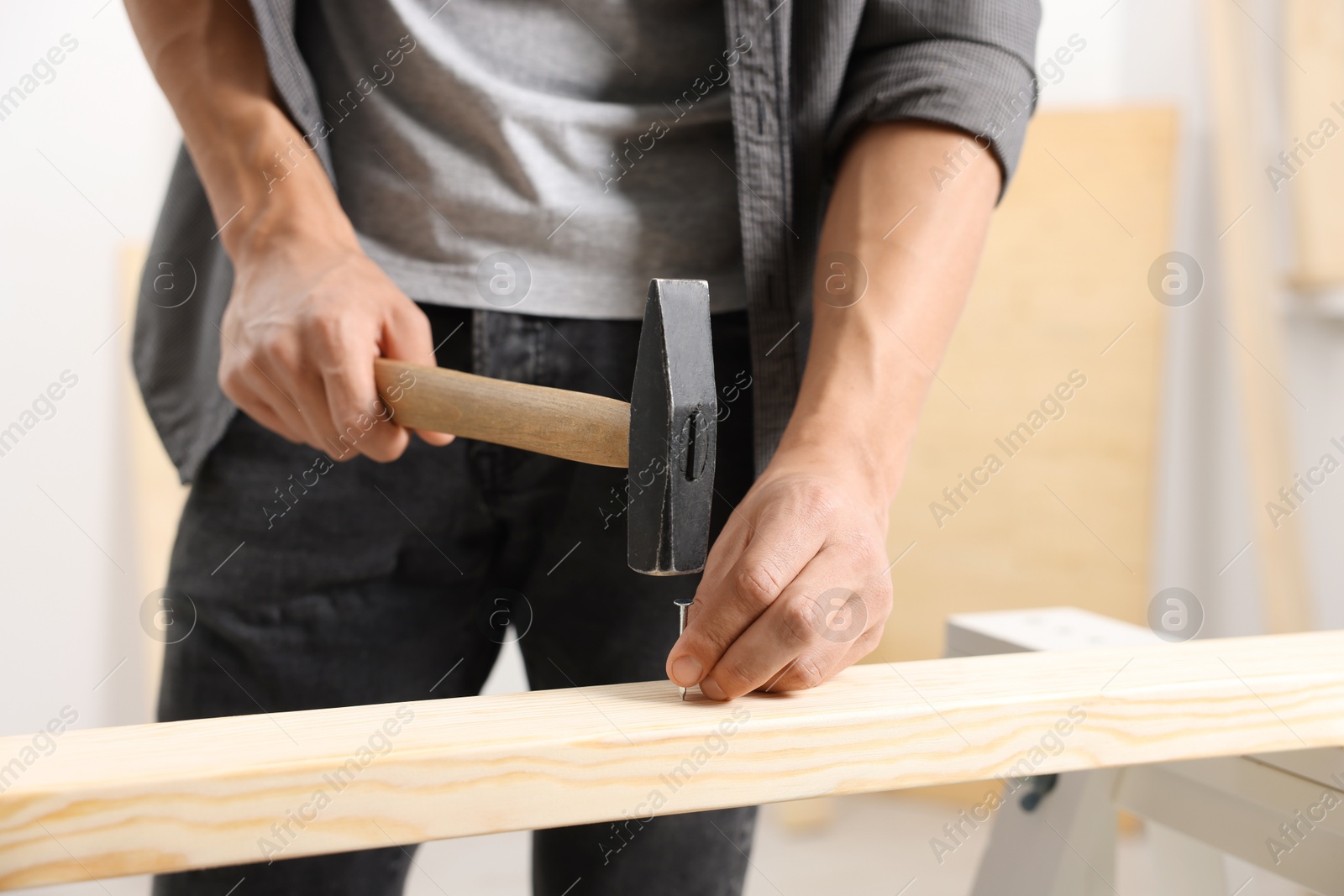 Man hammering nail into wooden plank indoors, closeup Photo of Man hammering nail into wooden plank indoors, closeup