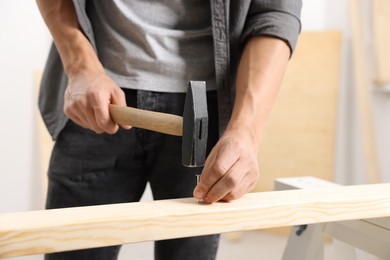 Photo of Man hammering nail into wooden plank indoors, closeup