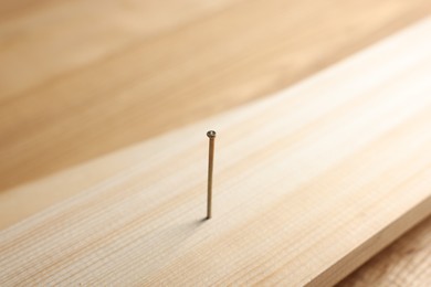 Photo of Metal nail in wooden plank on table, closeup