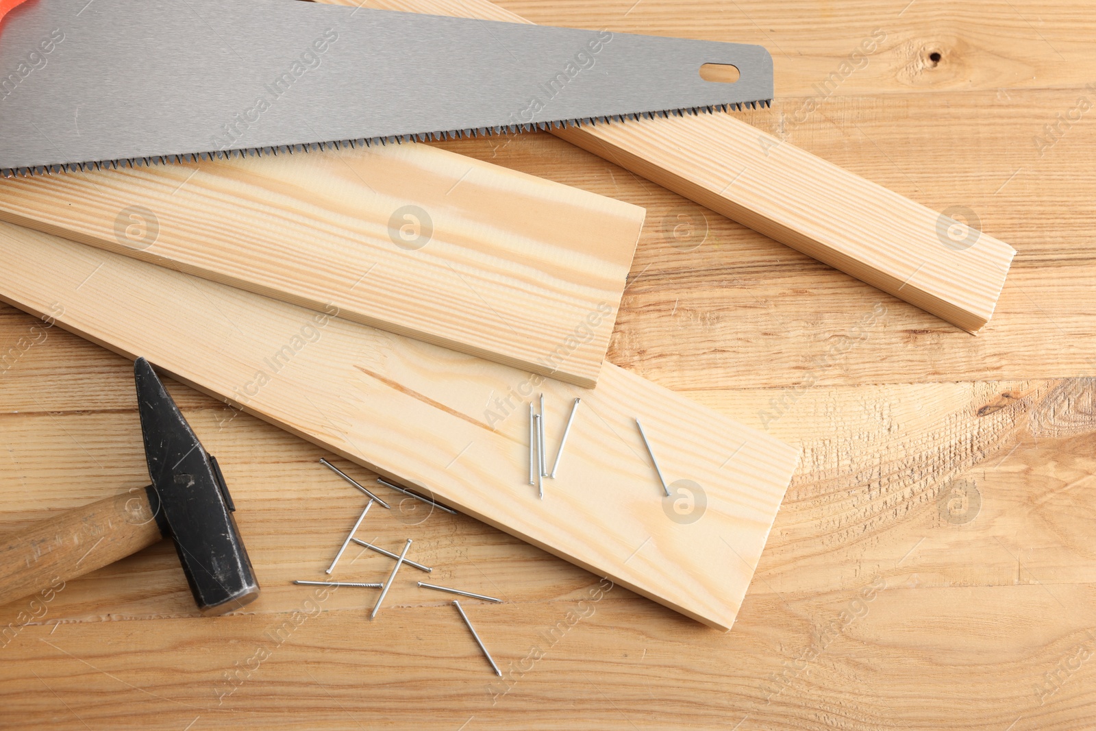 Photo of Metal nails, hammer, planks and saw on wooden table, flat lay