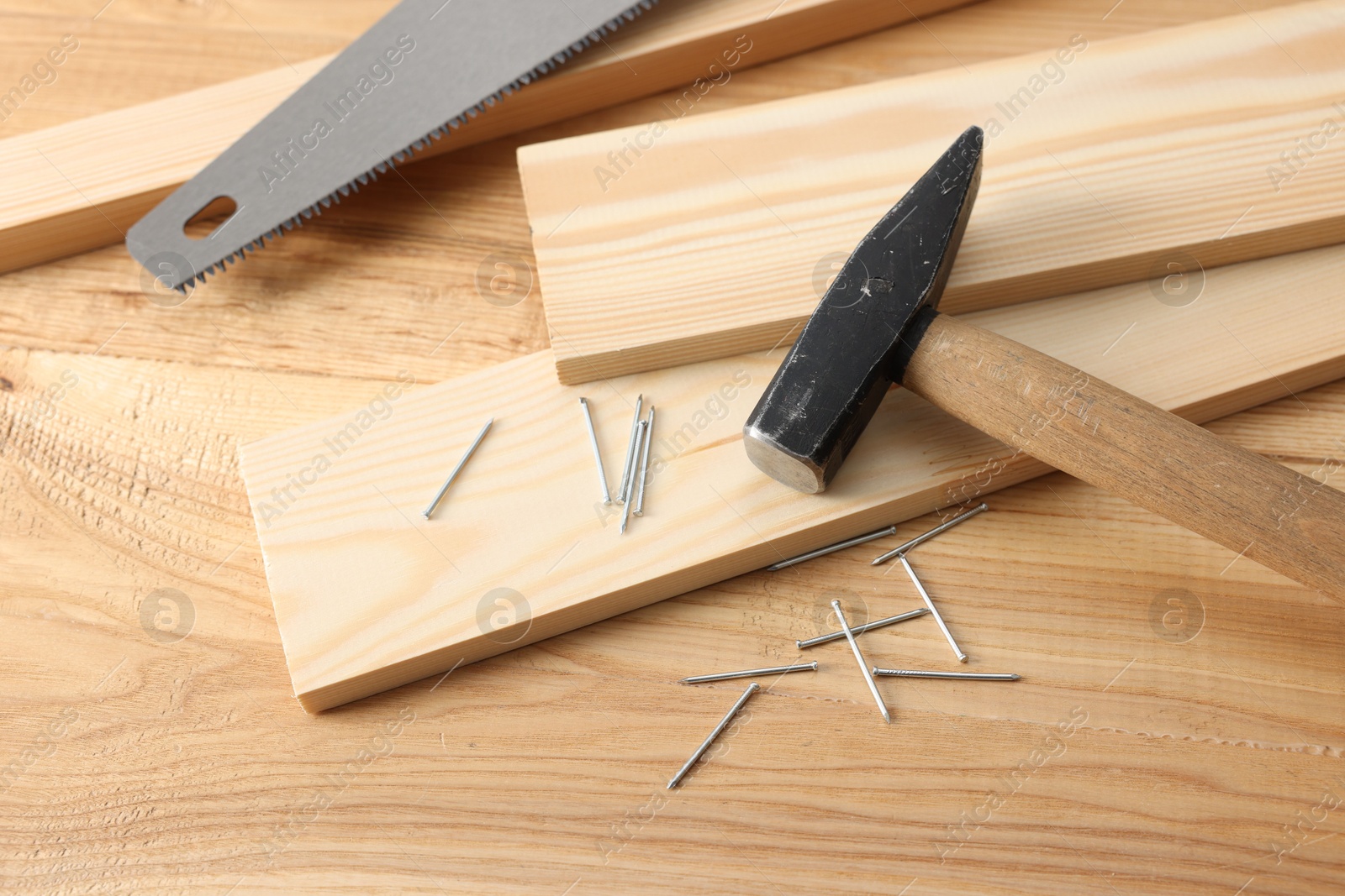 Metal nails, hammer, planks and saw on wooden table, above view Photo of Metal nails, hammer, planks and saw on wooden table, above view