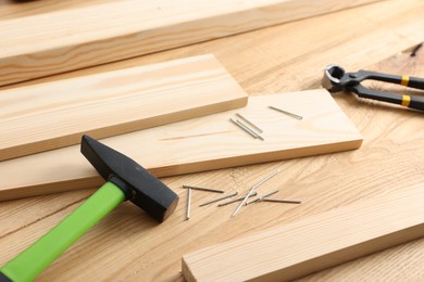 Photo of Metal nails, hammer, planks and pincers on wooden table, closeup