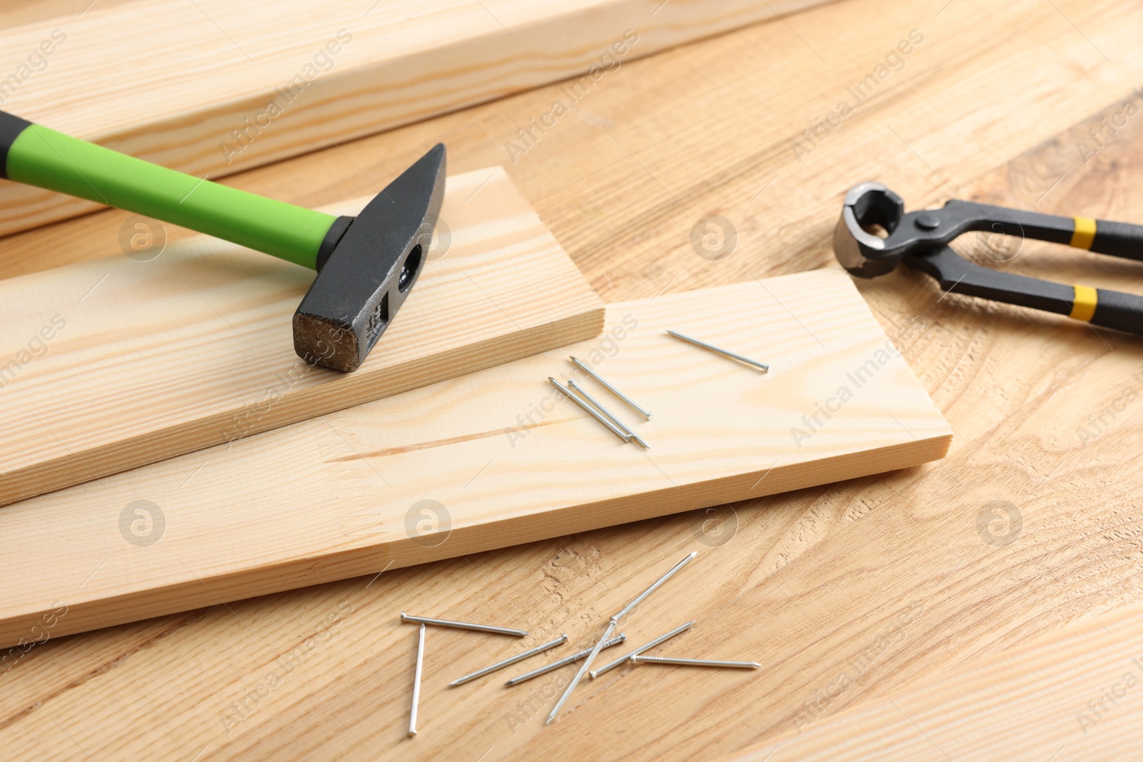 Metal nails, hammer, planks and pincers on wooden table, closeup Photo of Metal nails, hammer, planks and pincers on wooden table, closeup