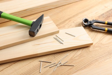 Photo of Metal nails, hammer, planks and pincers on wooden table, closeup