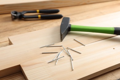 Photo of Metal nails, hammer, planks and pincers on wooden table, closeup