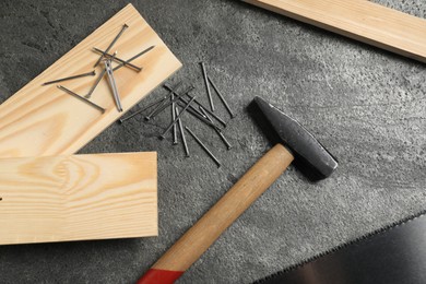 Photo of Metal nails, hammer, wooden planks and saw on grey table, flat lay