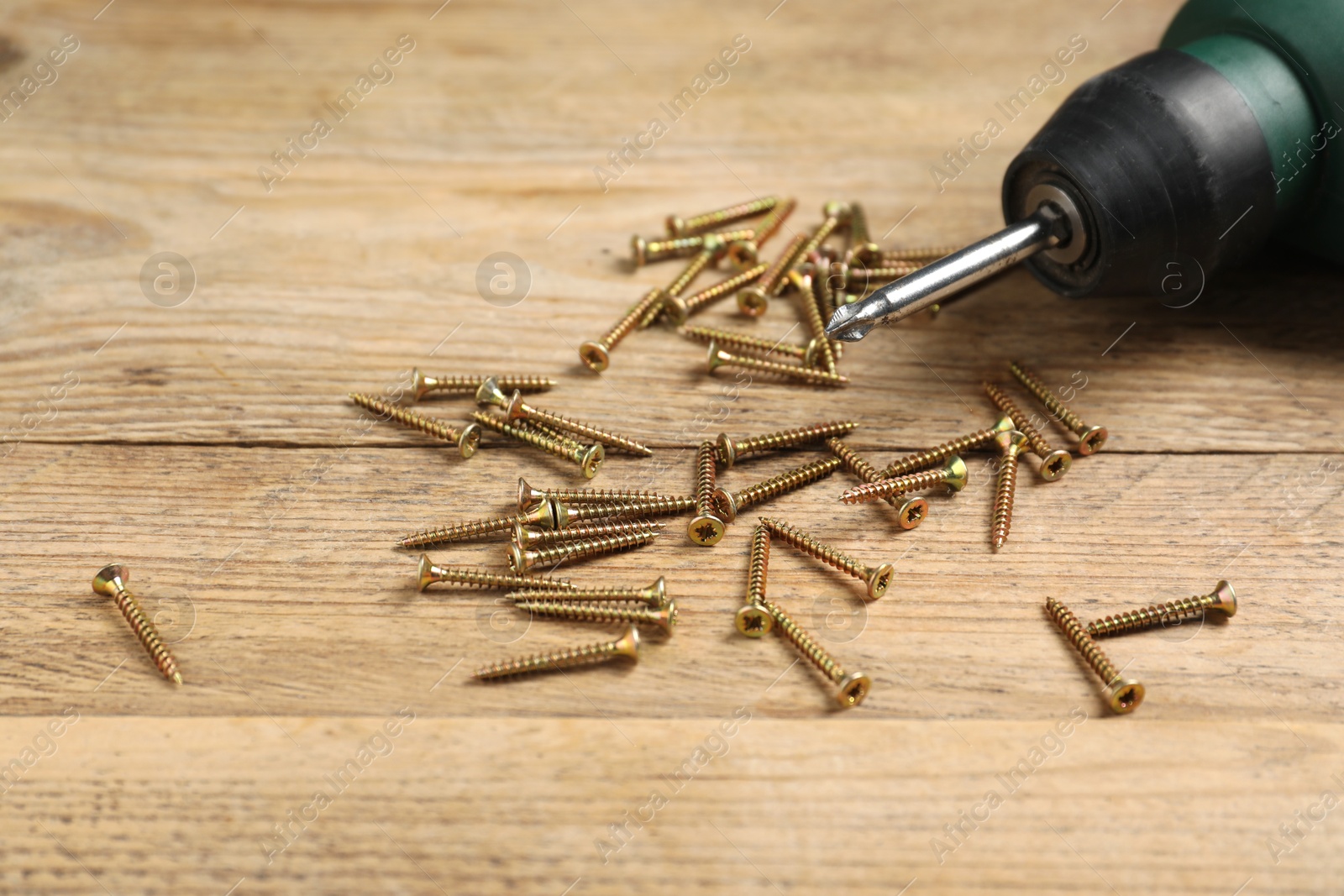 Photo of Many metal screws and electric screwdriver on wooden table, closeup. Space for text
