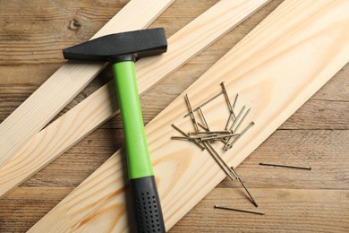 Photo of Hammer, metal nails and planks on wooden table, flat lay