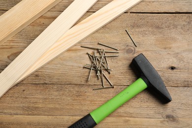 Photo of Hammer, metal nails and planks on wooden table, flat lay