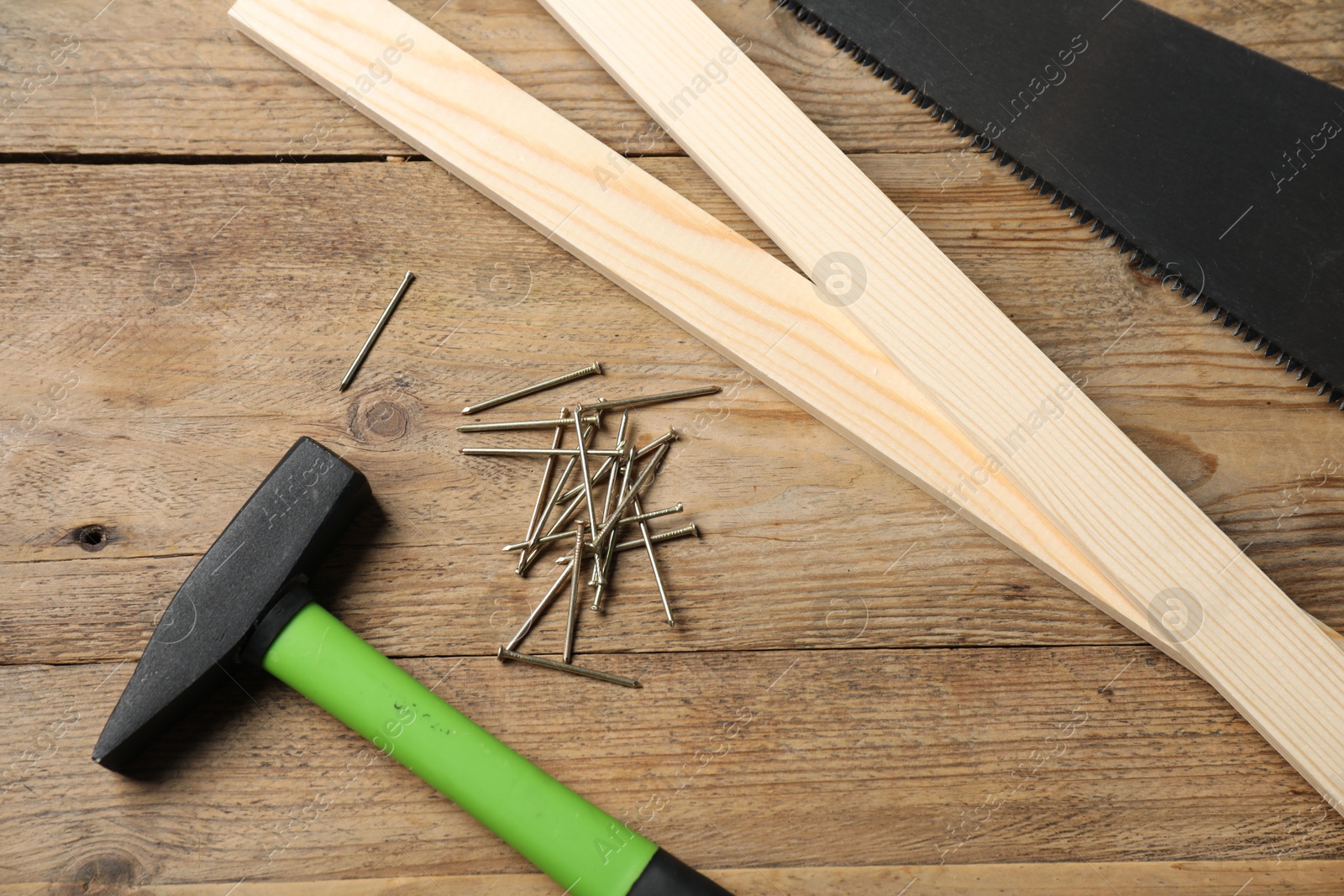 Photo of Metal nails, hammer, planks and saw on wooden table, flat lay