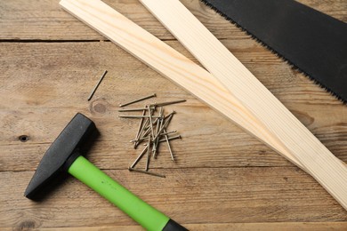 Photo of Metal nails, hammer, planks and saw on wooden table, flat lay
