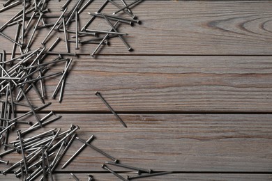 Photo of Many metal nails on wooden table, flat lay. Space for text