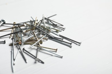 Photo of Different metal nails on white wooden table, closeup. Space for text