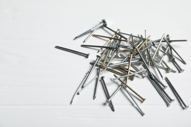 Photo of Different metal nails on white wooden table, closeup. Space for text