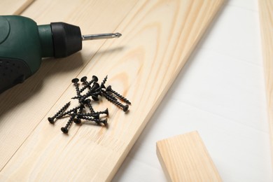 Photo of Many metal screws, electric screwdriver and wooden planks on white table, closeup