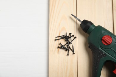 Photo of Many metal screws, electric screwdriver and wooden planks on white table, top view. Space for text