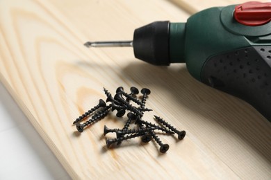 Photo of Many metal screws, electric screwdriver and wooden plank on white table, closeup