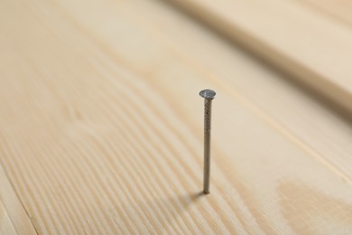 Photo of Metal nail in wooden plank on table, closeup. Space for text