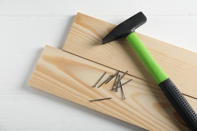 Photo of Hammer, metal nails and wooden planks on white table, flat lay
