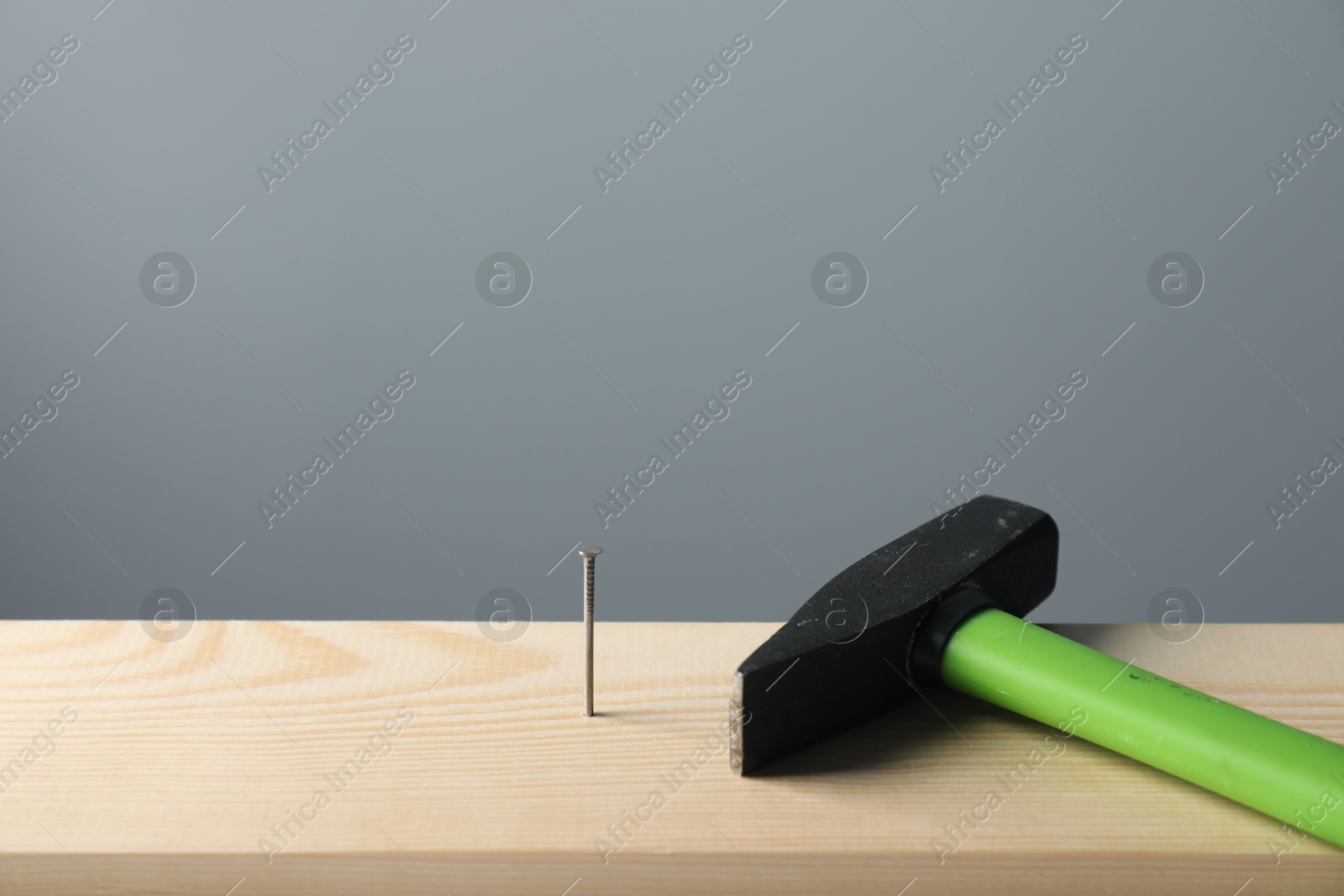Photo of Metal nail in wooden plank and hammer on grey background, closeup