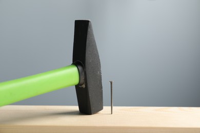 Photo of Metal nail in wooden plank and hammer on grey background, closeup