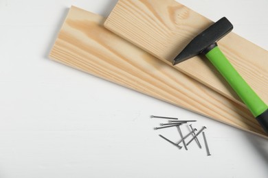Photo of Hammer, metal nails and wooden planks on white table, flat lay. Space for text
