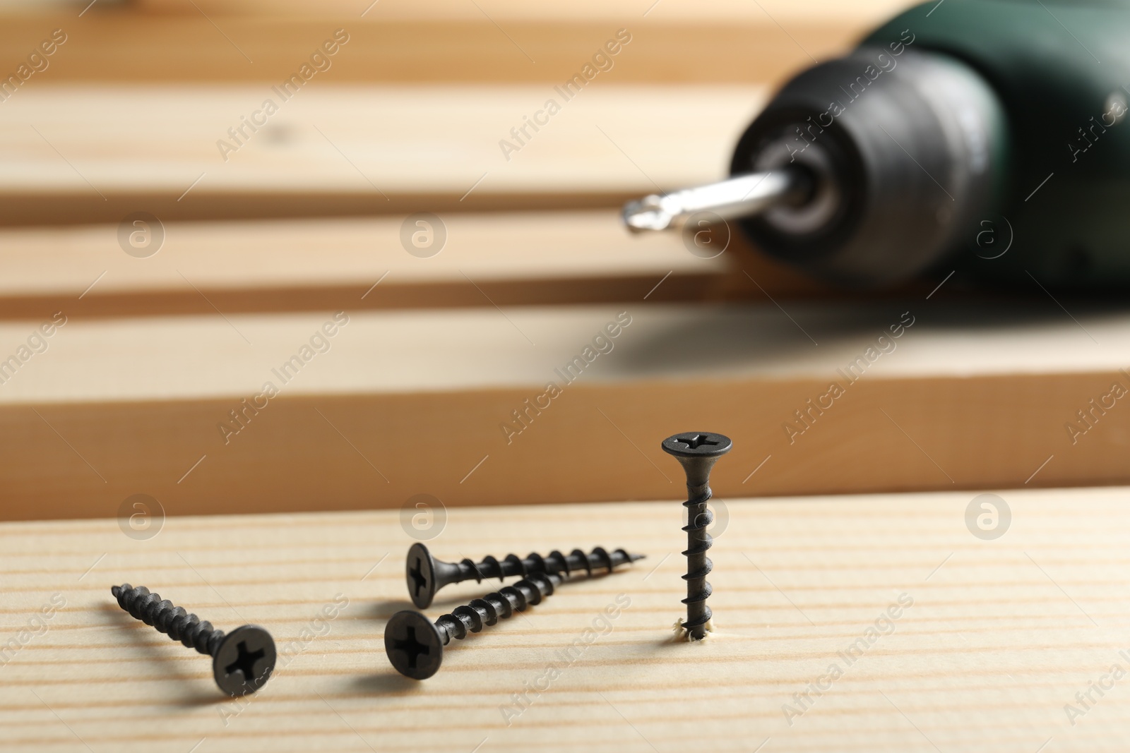 Metal screws, electric screwdriver and wooden planks on table, closeup Photo of Metal screws, electric screwdriver and wooden planks on table, closeup