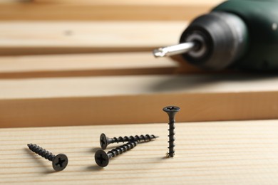 Photo of Metal screws, electric screwdriver and wooden planks on table, closeup
