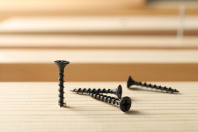Photo of Metal screws and wooden plank on table, closeup