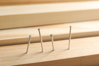 Photo of Metal nails in wooden plank on table, closeup