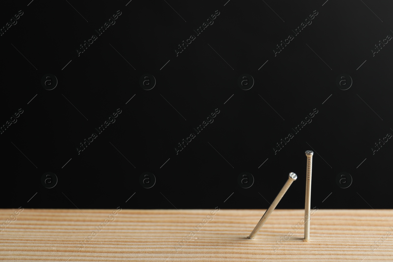Metal nails in wooden plank against black background, closeup. Space for text Photo of Metal nails in wooden plank against black background, closeup. Space for text