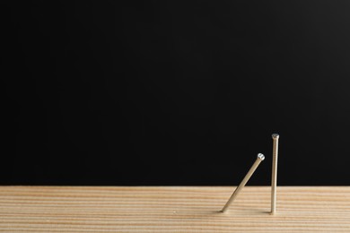 Photo of Metal nails in wooden plank against black background, closeup. Space for text