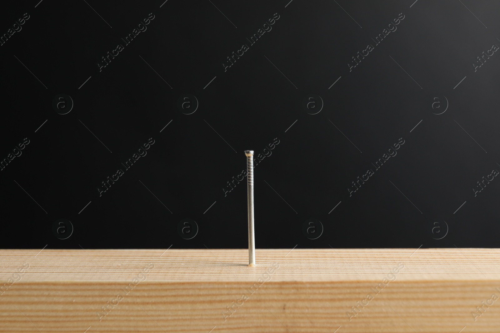 Metal nail in wooden plank against black background, closeup Photo of Metal nail in wooden plank against black background, closeup